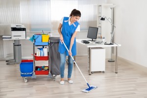 Full length portrait of happy female janitor mopping floor in office