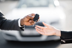 Car salesman handing over keys for new car to young woman against luxury auto